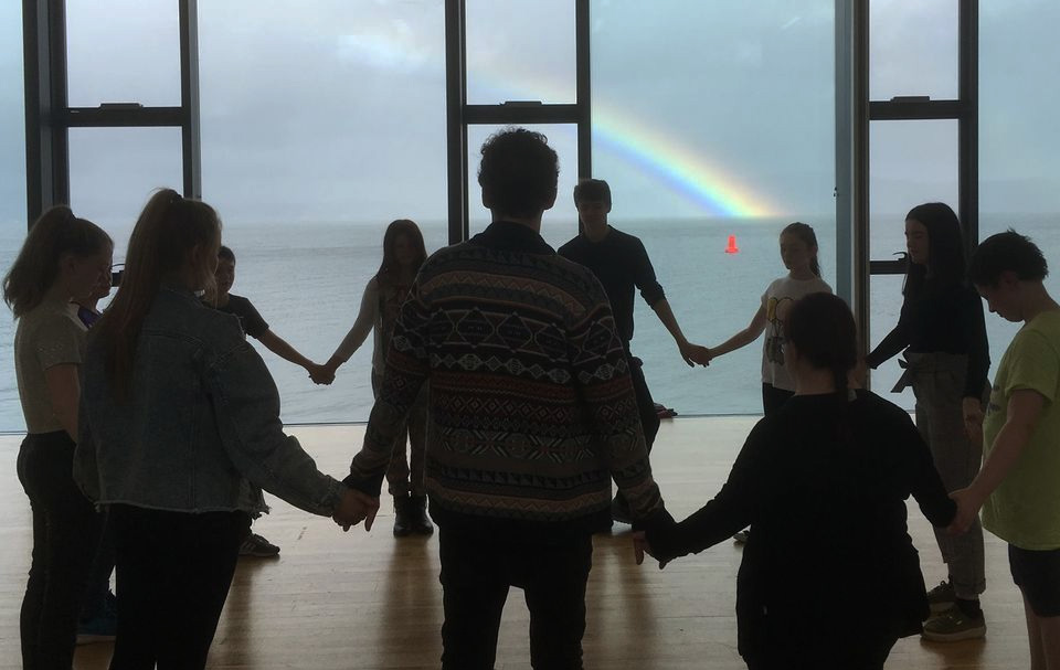 A circle of participants overlooking the Clyde estuary, with a rainbow behind.